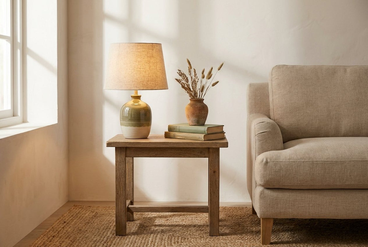 A linen-shaded table lamp glowing on a side table beside an armchair